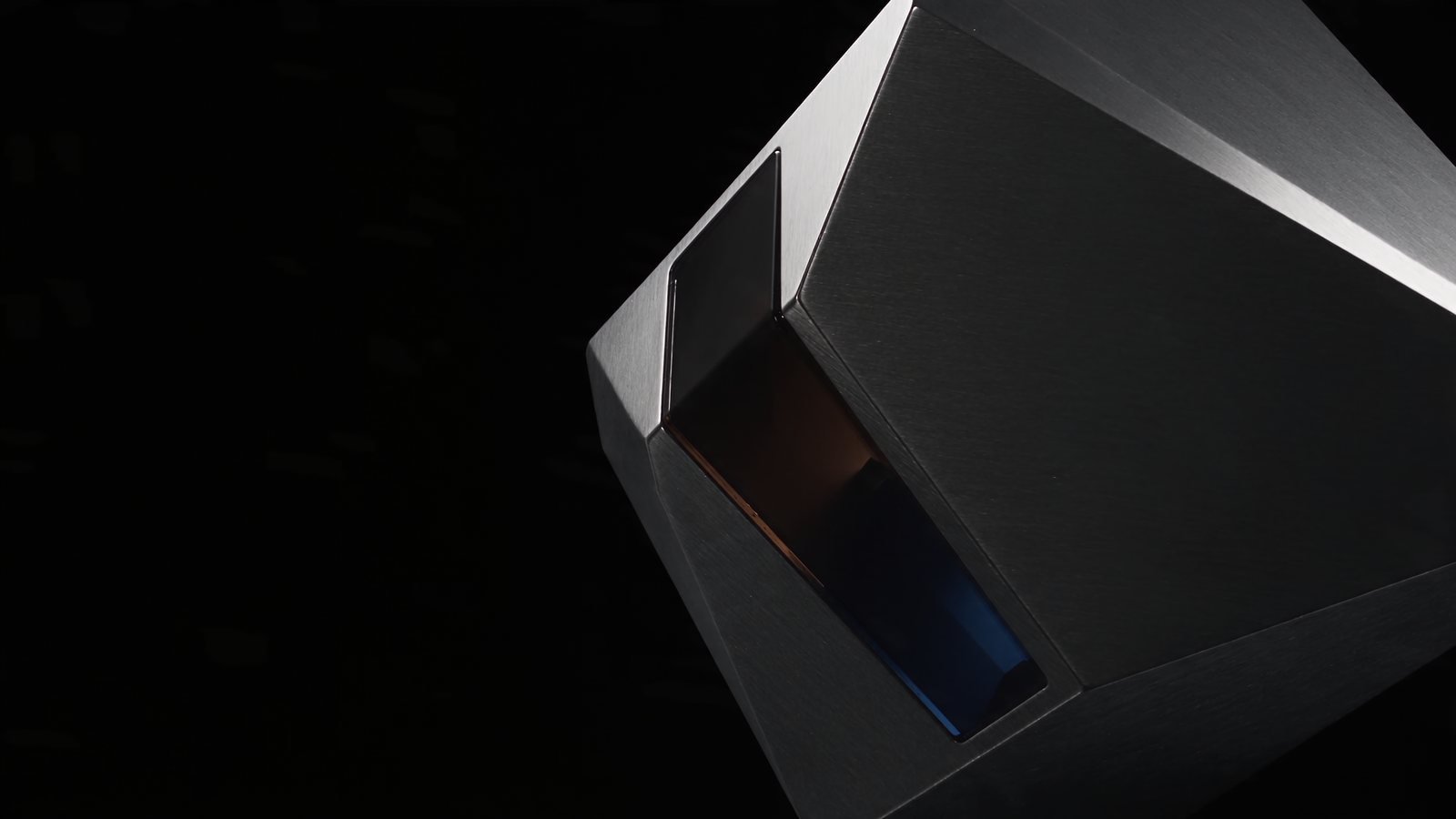A precision-machined black chrome form emerging from darkness, a recessed slot inside it glowing amber and cobalt.